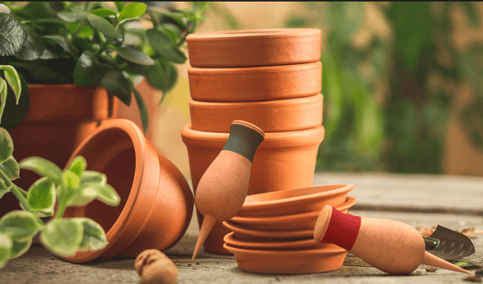 Stack of terracotta pots with self-watering stakes on a wooden surface, surrounded by green plants, ideal for spring planting and efficient watering.